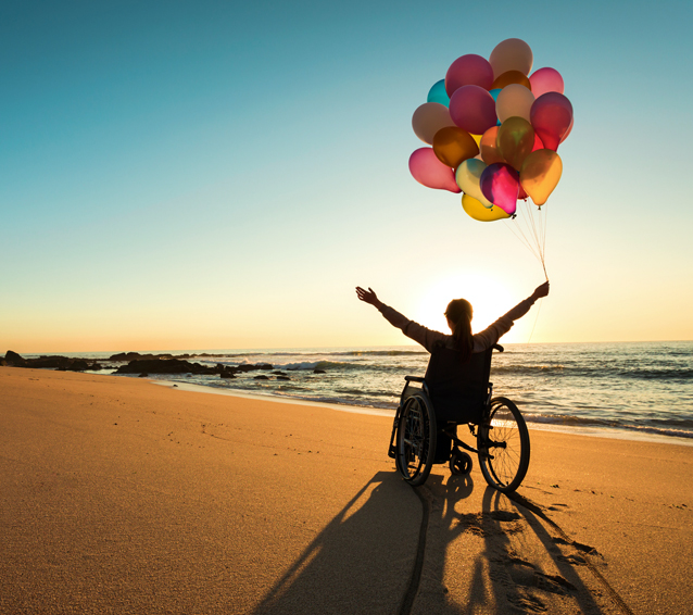 person in wheelchair on the beach with balloons signifying independence, freedom and happiness